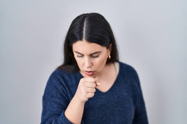 Genç esmer kadın izole edilmiş arka planda duruyor kendini kötü hissediyor ve soğuk algınlığı veya bronşitin belirtisi olarak öksürüyor. sağlık hizmeti kavramı. 