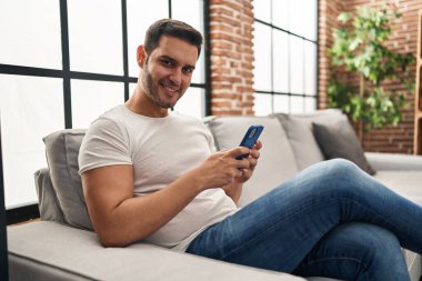 Evdeki kanepede oturan, akıllı telefon kullanan genç bir İspanyol.
