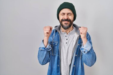 Young hispanic man with tattoos wearing wool cap excited for success with arms raised and eyes closed celebrating victory smiling. winner concept. 