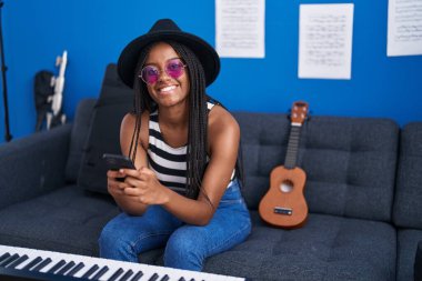 Müzik stüdyosunda akıllı telefon kullanarak gülümseyen Afrikalı Amerikalı kadın müzisyen.