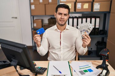 Küçük işletme şirketinde sakallı genç İspanyol bir adam elinde banknotlar ve kredi kartından bihaber ve kafası karışık bir ifade tutuyordu. şüphe kavramı. 