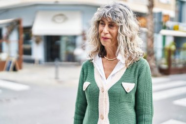 Orta yaşlı bir kadın sokakta kendine güvenerek gülümsüyor.