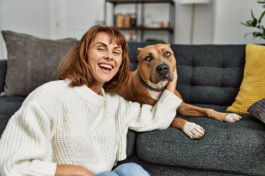 Beyaz kadın gülümsüyor. Kendine güvenen, kucaklayan köpek evde yerde oturuyor.