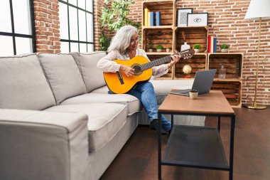 Orta yaşlı bir kadının evde online gitar dersi var.