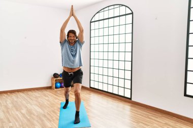 Orta yaşlı beyaz bir adam spor merkezinde yoga eğitimi alırken gülümsüyor.
