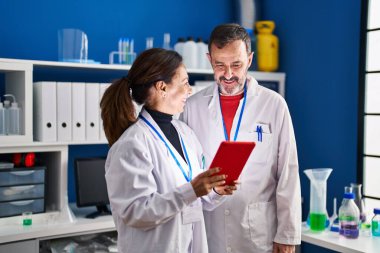 Orta yaşlı erkek ve kadın bilim adamları laboratuarda çalışan touchpad kullanıyorlar.