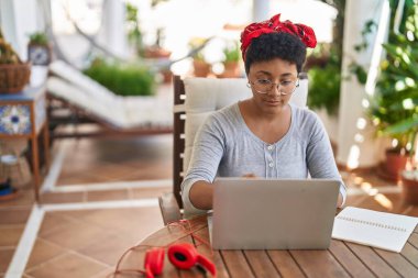 Afro-Amerikalı bir kadın evdeki terasta oturmuş ders çalışıyor.