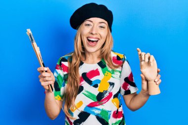 Beyaz kadın sanatçı elinde küçük ahşap manikinler ve boya fırçaları tutarak gülüyor ve kahkahalarla gülüyor.. 