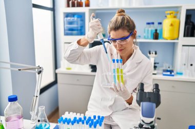 Laboratuvarda pipet kullanan bilim adamı üniforması giyen genç sarışın kadın.