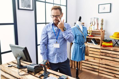 Middle age man working as manager at retail boutique pointing to the eye watching you gesture, suspicious expression 