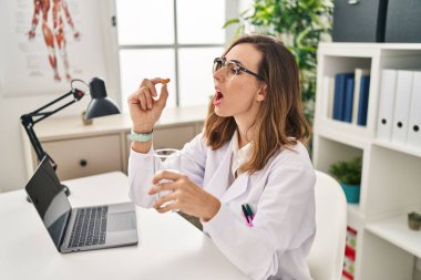 Young woman wearing doctor uniform taking pills at clinic