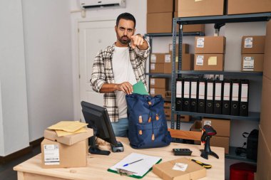 Küçük işletme şirketinde çalışan sakallı genç İspanyol bir adam kamerayı işaret ediyor ve kendine güveni tam bir jest yapıyor. 