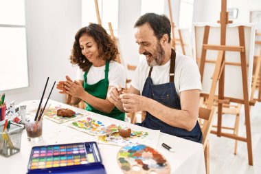 Sanat okulundaki masada oturan mutlu mankenlik kiline gülümseyen iki orta yaşlı öğrenci..