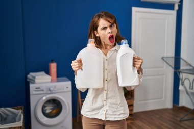 Şok olmuş yüzünde deterjan şişeleri tutan genç ve güzel bir kadın şüpheci ve alaycı görünüyor. 