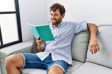 Evdeki kanepede oturmuş kitap okuyan genç bir İspanyol..