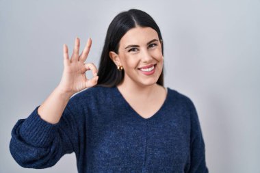 Genç esmer kadın izole edilmiş arka planda durup gülümsüyor ve el ve parmaklarıyla 