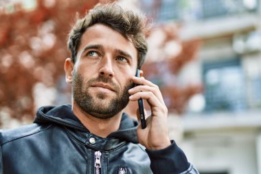 Handsome hispanic man with beard with serious face outdoors speaking on the phone