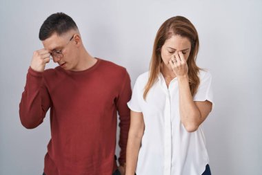 Mother and son standing together over isolated background tired rubbing nose and eyes feeling fatigue and headache. stress and frustration concept. 