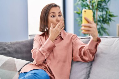 Orta yaşlı bir kadın evdeki koltukta oturmuş video görüşmesi yapıyor.