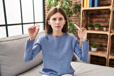 Young brunette woman holding menstrual cup and tampon relaxed with serious expression on face. simple and natural looking at the camera. 