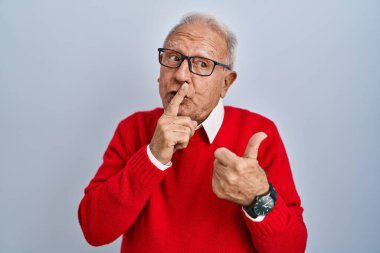 İzole edilmiş arka planda gri saçlı yaşlı bir adam sessiz olmak istiyor. Parmakları dudaklarında, elleri yana doğru işaret ederek. sessizlik ve gizli konsept. 