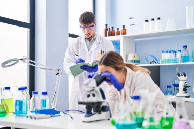Young man and woman scientists workers using microscope at laboratory