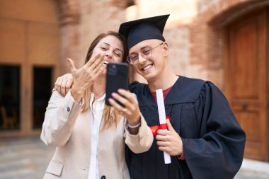 Erkek ve kadın anne ve mezun oğul birbirlerine sarılıyorlar üniversitede video görüşmesi yapıyorlar.