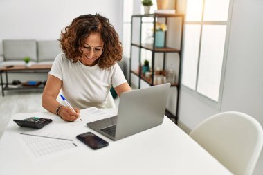 Orta yaşlı İspanyol kadın evde çalışırken kendine güvenerek gülümsüyor.