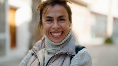 Orta yaşlı İspanyol kadın sokakta kendine güvenerek gülümsüyor.