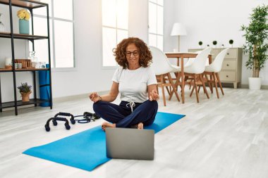 Olgun İspanyol kadın vücut kaslarını esneterek evdeki oturma odasında özel ders videolarına bakıyor.