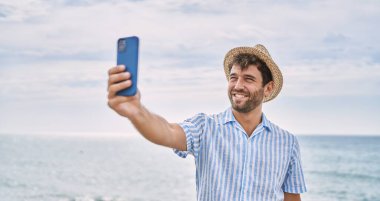 Genç İspanyol gülümseyen adam sahildeki akıllı telefonun yanında selfie çekerken mutlu oluyor.