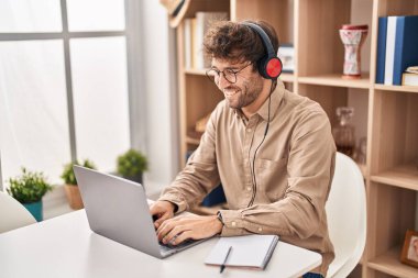 Ofiste çalışan genç bir iş adamı dizüstü bilgisayar ve kulaklık kullanıyor.