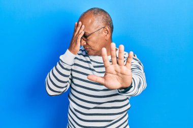 Orta yaşlı Latin bir adam gündelik kıyafetler giyiyor ve gözlük takıyor. Gözlerini elleriyle kapatıyor ve üzgün ve korku ifadeleriyle jestleri durduruyor. utangaç ve olumsuz kavram. 