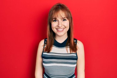 Yüzünde mutlu ve havalı bir gülümseme olan gündelik tişört giyen kızıl saçlı genç bir kadın. şanslı kişi. 