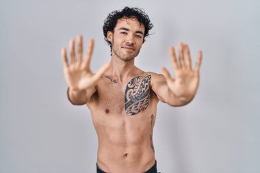 Hispanic man standing shirtless showing and pointing up with fingers number ten while smiling confident and happy. 