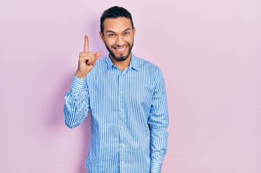 Hispanic man with beard wearing casual blue shirt pointing finger up with successful idea. exited and happy. number one. 