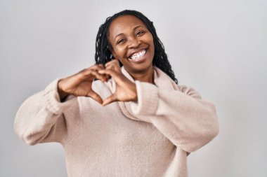 Beyaz arka planda dikilen Afrikalı bir kadın. Sevgiyle gülümsüyor. Elleriyle kalp sembolü yapıyor. romantik kavram. 