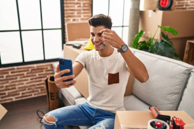 Young hispanic man having video call holding key of house at new home