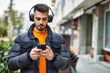 Yakışıklı, sakallı, mutlu ve kendine güvenen, akıllı telefon kullanan, kışlık palto giyen bir İspanyol.