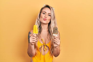 Beautiful young blonde woman wearing summer swimsuit holding ice creams looking at the camera blowing a kiss being lovely and sexy. love expression. 