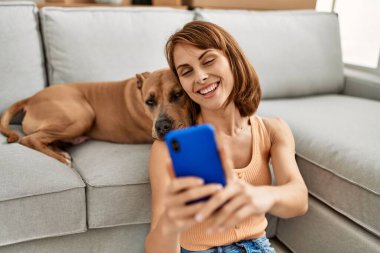 Kafkasyalı genç bir kadın akıllı telefonun yanında evde köpekle oturmuş selfie çekiyor.