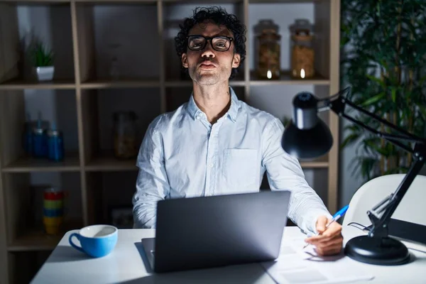 Hispanic man working at the office at night looking at the camera blowing a kiss on air being lovely and sexy. love expression.