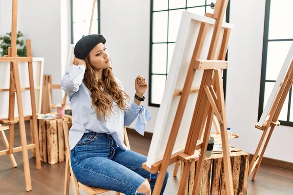 若いヒスパニック系のアーティストの女性がアートスタジオでキャンバスに絵を描くことは 質問を混乱させ 疑問に思う 疑いもなく頭に手を置いて考える 包括的な概念は — ストック写真