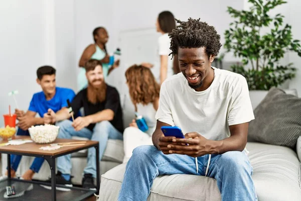 Group of young friends smiling happy sitting on the sofa. Woman using smartphone at home.