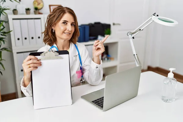 Médico Mediana Edad Mujer Sujetando Portapapeles Con Espacio Blanco Sonriendo —  Fotos de Stock