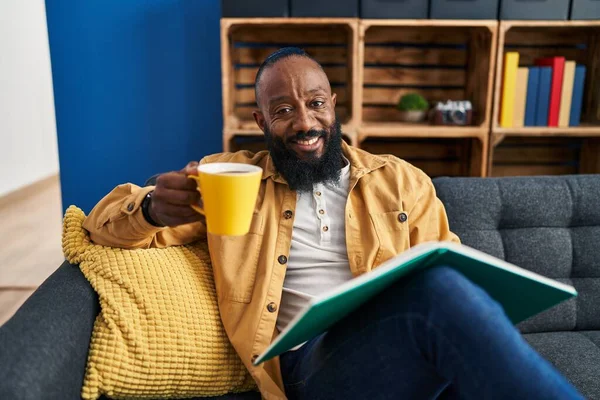 Young African American Man Reading Book Drinking Coffee Home — стоковое фото