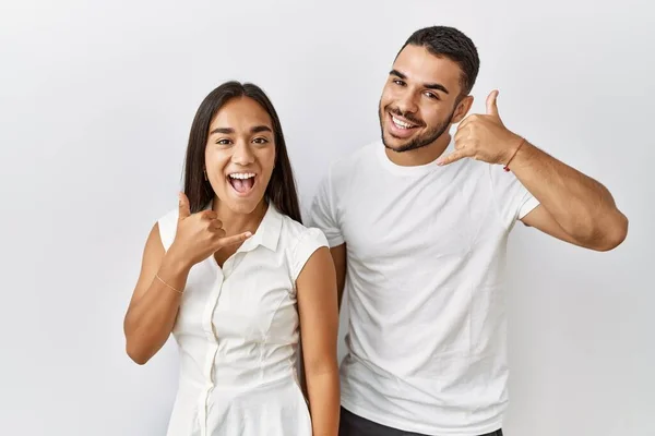 Young interracial couple standing together in love over isolated background smiling doing phone gesture with hand and fingers like talking on the telephone. communicating concepts.