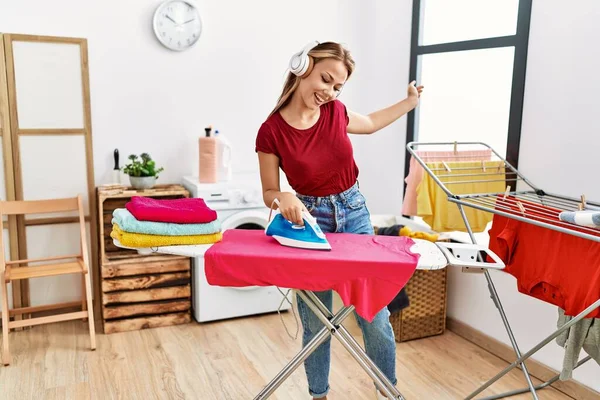 Young Caucasian Girl Ironing Clothes Listening Music Home — стоковое фото