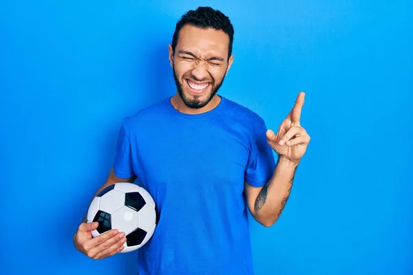 Hispanic Man Beard Holding Soccer Ball Gesturing Finger Crossed Smiling — 스톡 사진