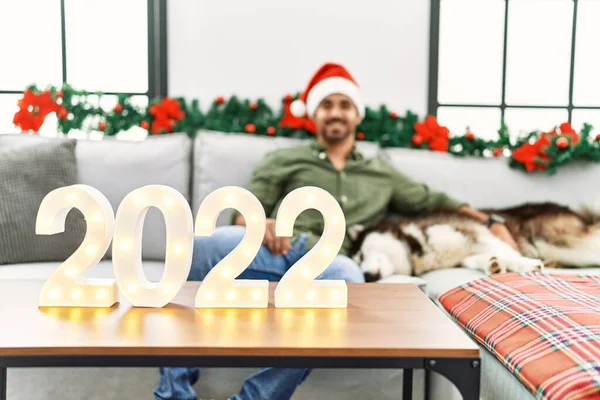 Young hispanic man hugging dog celebrate new year sitting by christmas decor at home